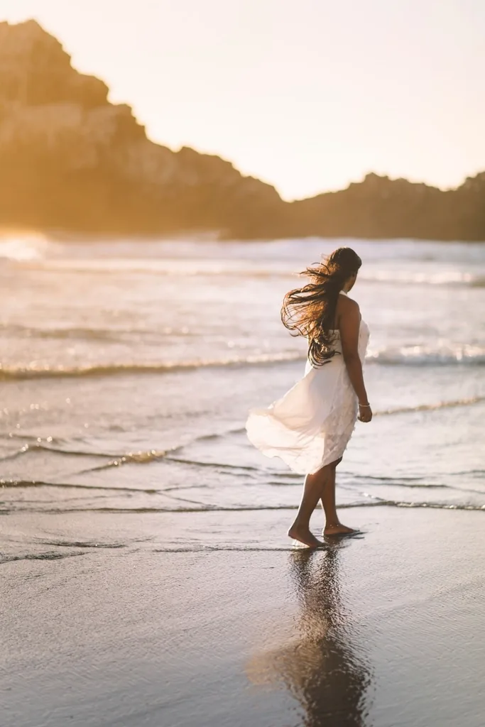 Mujer con vestido blanco de lino caminando en la orilla al atardecer