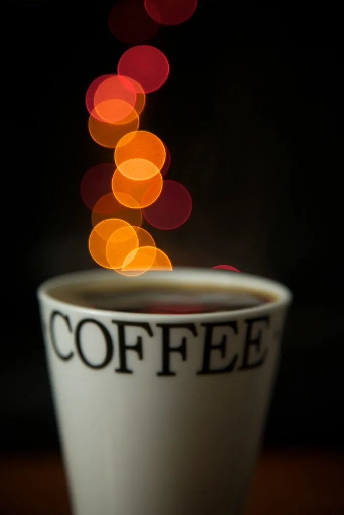 Taza de café frente a luces cálidas desenfocadas en la oscuridad